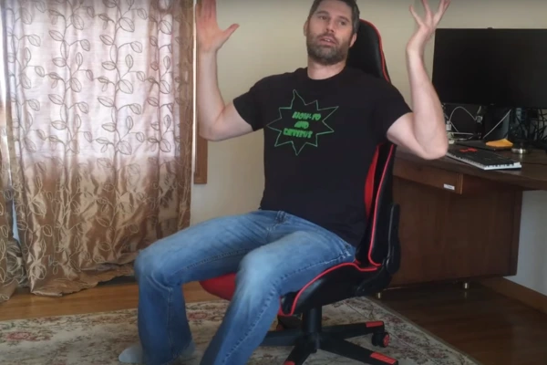 A frustrated man sits on a gaming chair, hands raised in exasperation, addressing the issue of the chair sinking.